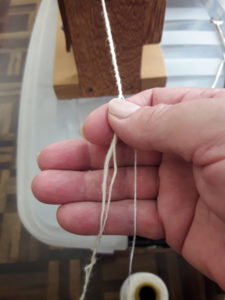 2 fios de espessuras diferentes no mesmo projeto. Foto da mão direita de Isaura Mattos equilibrando fio artesanal torcido em roca elétrica.