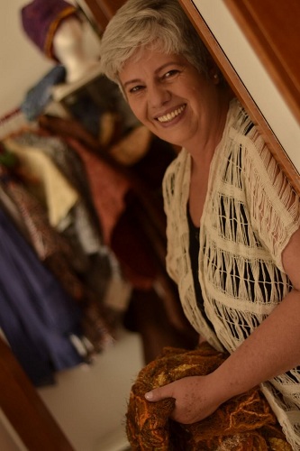 Foto de Isaura Mattos em pé, com ombro direito encostado no batente de uma porta, sorrindo para você.
