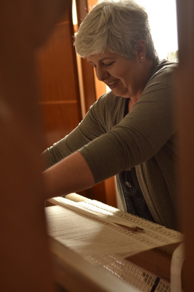 Comecei a Tecer: Como a Tecelagem Mudou Minha Vida — e Pode Mudar a SuaTecelagem e Aposentadoria. Sempre tecendo; sempre aprendendo 3 Vantagens Neurológicas da Tecelagem Manual. Foto de peça ainda presa em tear. Foto ilustrativa mostra Isaura Mattos fazendo renda no tear de pedal. Tecelagem Manual em curso online . Isatramas site página Home